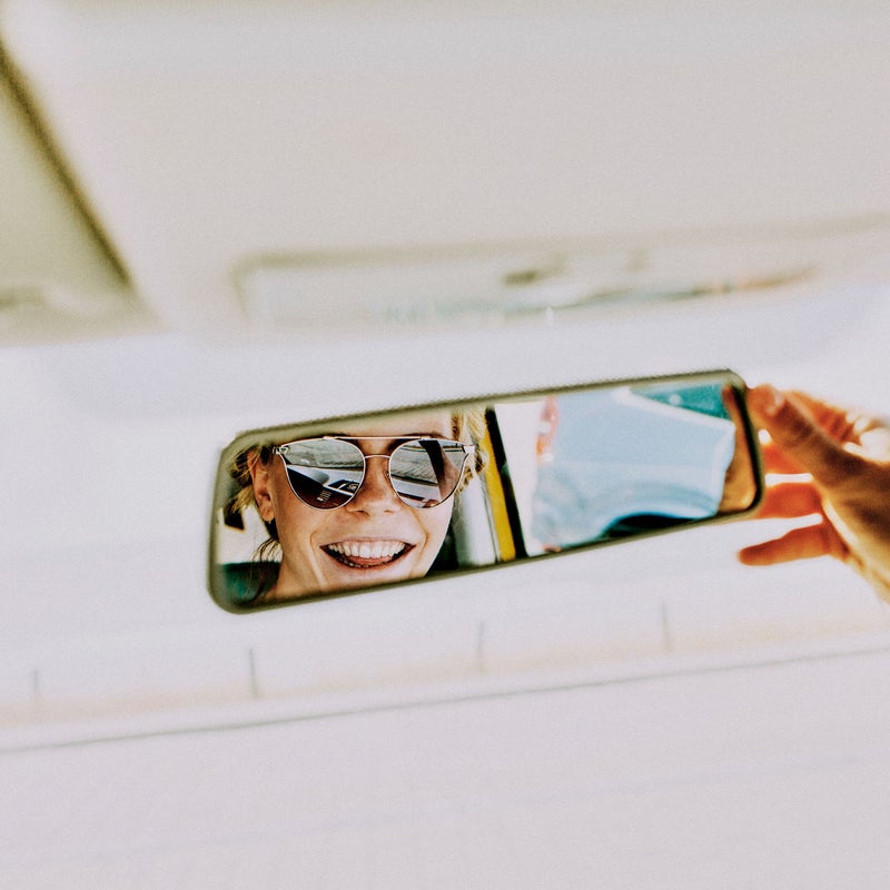 Chica con gafas de sol mirándose en el retrovisor.