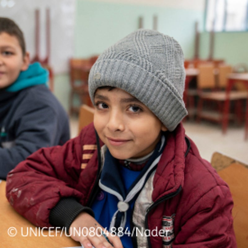 Un niño pequeño con gorro sentado en una clase y un compañero al lado