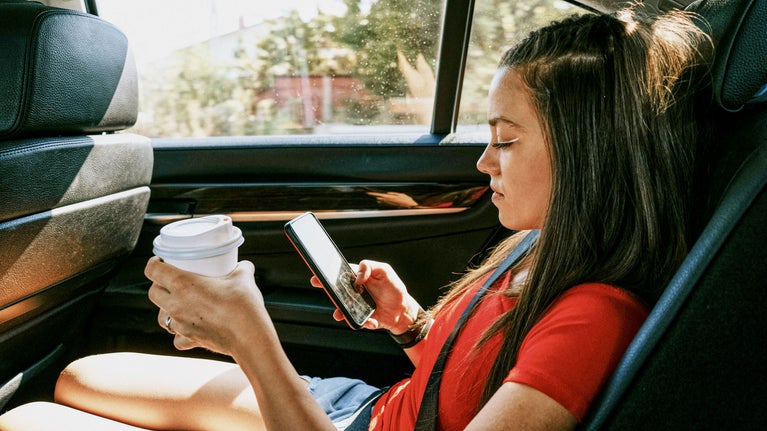 Chica en un coche con el movil y un café
