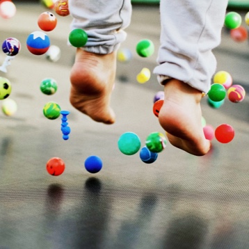 Pies de un niño saltando en una cama elástica con pelotas de colores