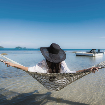 Chica de esoaldas en una hamaca con el mar de fondo