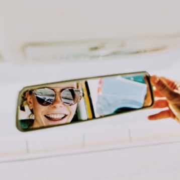 Chica con gafas de sol mirándose en el retrovisor.
